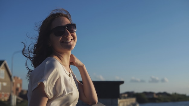 Hermosa chica disfruta de la puesta de sol en el paseo marítimo y sonriendo a la cámara