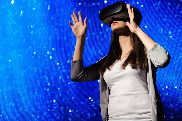 Una hermosa chica con un dispositivo de realidad virtual, de pie en el fondo del cielo.