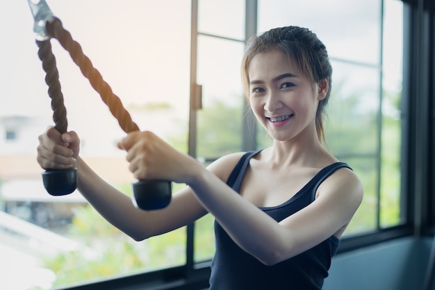 Hermosa chica ejercicios tirando de la cuerda para fortalecer los músculos en el gimnasio público