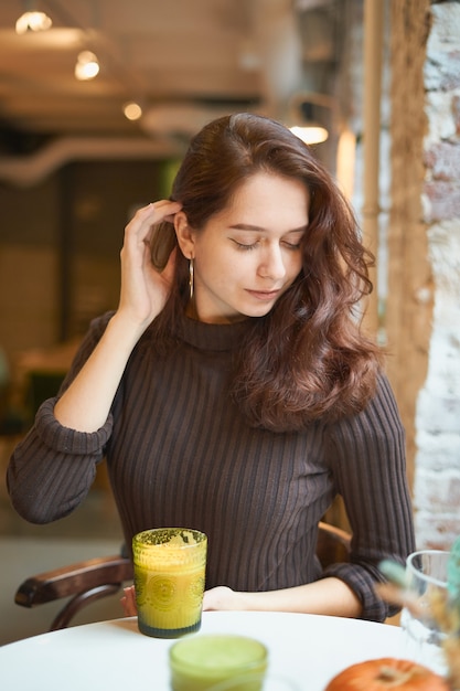 Hermosa chica elegante moda elegante elegante está sentado en la cafetería y beber batido saludable