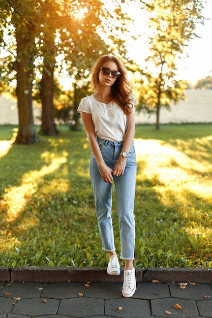 Hermosa chica elegante en ropa de moda se encuentra en el parque en un día soleado