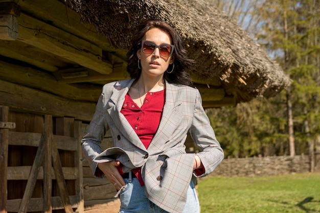 Una hermosa chica elegantemente vestida con el telón de fondo de una antigua casa rural bajo un techo de paja.