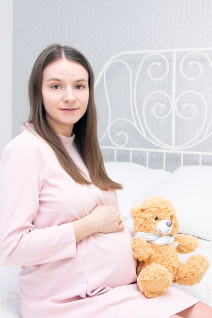 Hermosa chica embarazada está sentada en la cama y sus manos están sobre su estómago. concepto de embarazo, maternidad, preparación y expectativa.