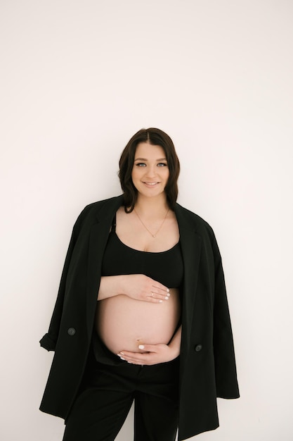 Hermosa chica embarazada con rizos en un traje negro sobre un fondo blanco el concepto de un feliz embarazo y familia