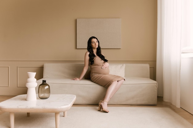 Hermosa chica embarazada con rizos en un vestido en un estudio luminoso con un interior elegante el concepto de un feliz embarazo y familia