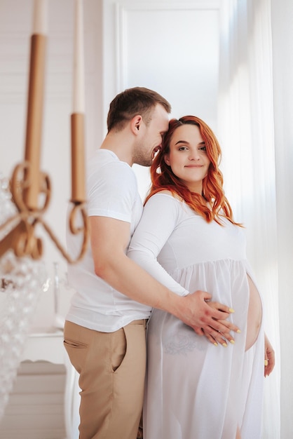 Hermosa chica embarazada en vestido blanco con marido en estudio