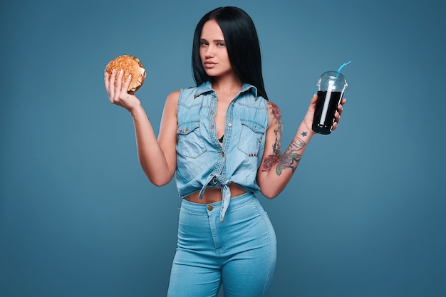 Hermosa chica encantadora del tatuaje con hamburguesa y refresco