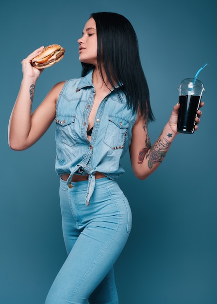 Hermosa chica encantadora del tatuaje con hamburguesa y refresco