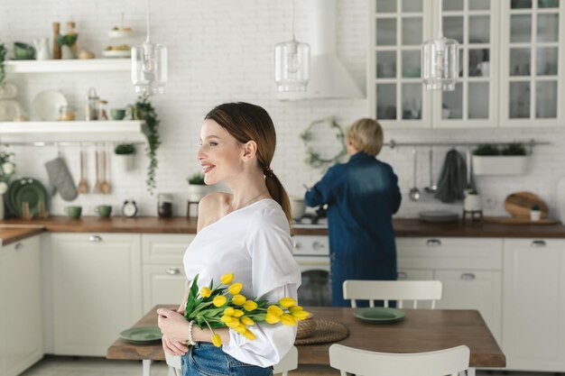 Foto hermosa chica se encuentra en la cocina y tiene tulipanes en sus manos día de la mujer 8 de marzo