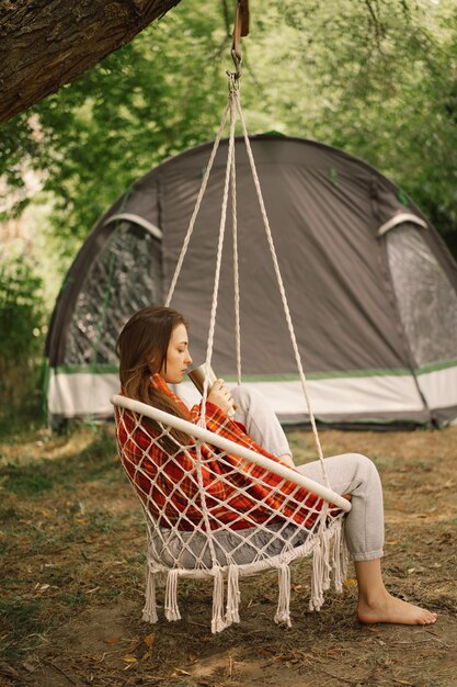 Hermosa chica envuelta en cuadros rojos bebiendo té en una acogedora silla colgante al aire libre viajes de aventura