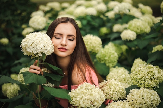 Hermosa chica está en arbustos de flores de hortensias en el jardín al atardecer. Flores en las calles de la ciudad.