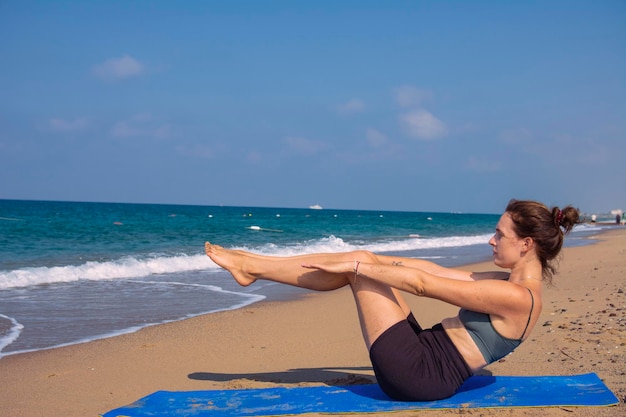 Una hermosa chica está haciendo yoga en la playa cerca del mar.