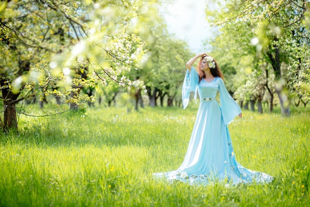 Hermosa chica está de pie en el jardín de manzanas de primavera con un vestido largo