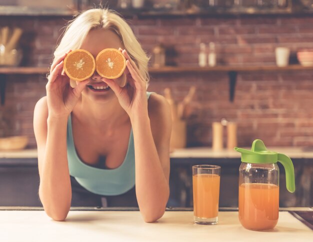 Hermosa chica está sosteniendo rodajas de naranja en sus ojos