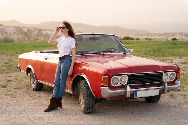 Hermosa chica en estilo retro posando cerca de un coche descapotable rojo vintage