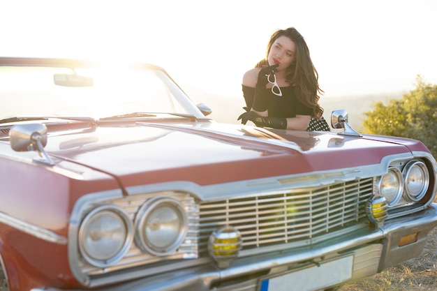 Foto hermosa chica en estilo retro posando cerca de un coche descapotable rojo vintage