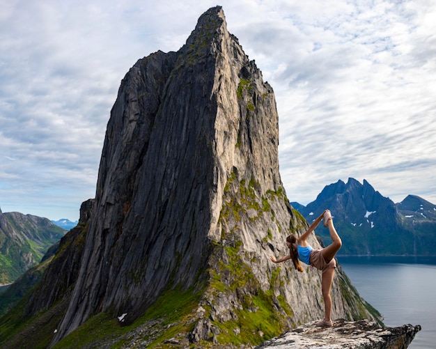 hermosa chica se estira (yoga - posición de bailarina) sobre rocas con vistas a la famosa montaña segla, noruega