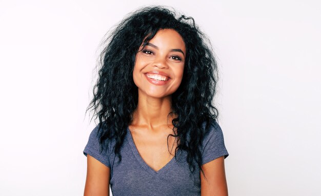 Hermosa chica de etnia africana con amplia sonrisa sincera y fascinantes ojos oscuros está mirando a la cámara y sonriendo