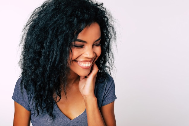 Hermosa chica de etnia africana con amplia sonrisa sincera y fascinantes ojos oscuros está mirando a la cámara y sonriendo