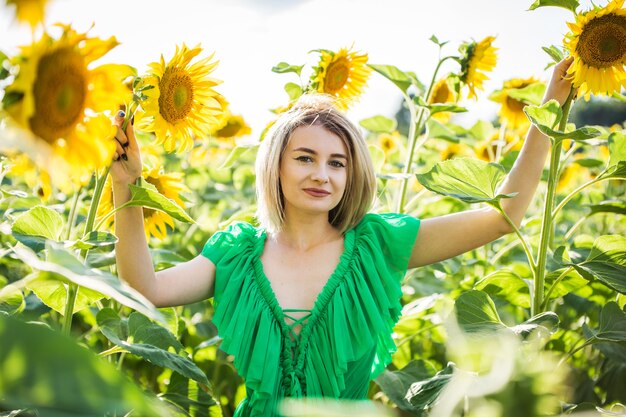 Hermosa chica europea con un vestido verde en la naturaleza con girasoles