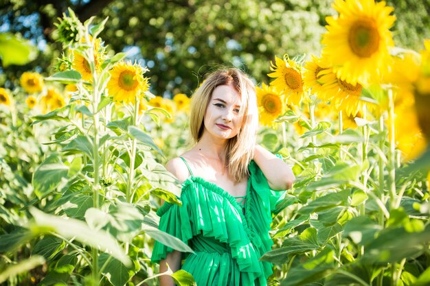 Hermosa chica europea con un vestido verde en la naturaleza con girasoles