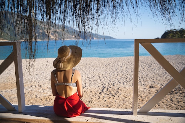 Hermosa chica con falda roja y sombrero en verano en una terraza a orillas del mar