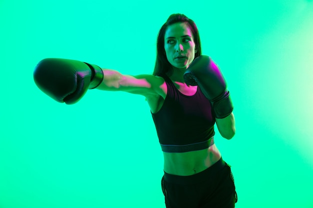 Hermosa chica de fitness joven confiada que se encuentran aisladas sobre la pared de neón verde, boxeo