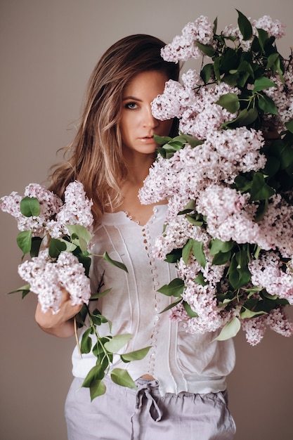 Hermosa chica con flores lilas en sus manos. Una niña con flores lilas en la primavera en casa. Una niña de cabello largo y lila en sus manos.