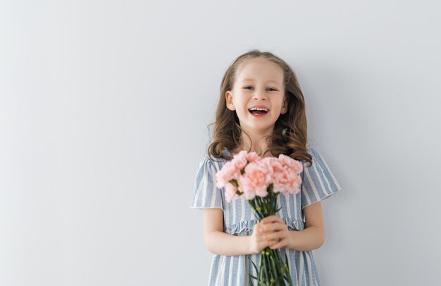 Hermosa chica con flores rosas en las manos sobre fondo de pared gris