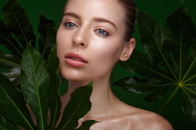 Hermosa chica fresca con maquillaje natural de piel perfecta y hojas verdes Rostro de belleza