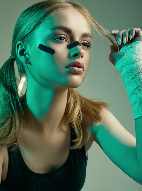 Hermosa chica fuerte con cabello rubio, mirada segura, puños en vendas protectoras de boxeo