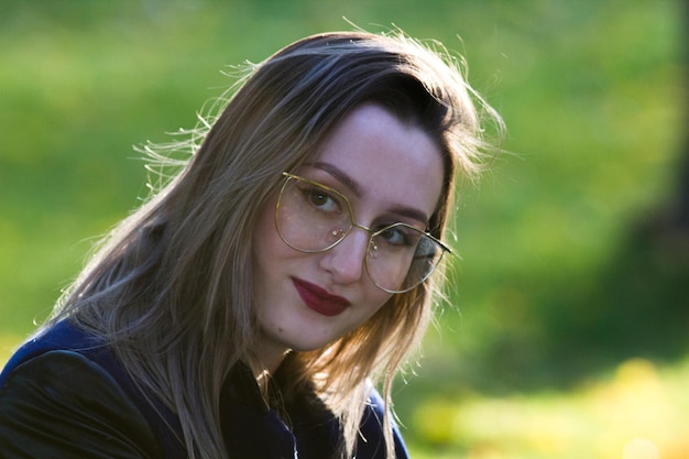 Hermosa chica en gafas con lápiz labial rojo mirando a la cámara iluminación de contorno natural