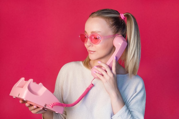 Hermosa chica con gafas rosas hablando por un teléfono fijo con un receptor de estilo retro