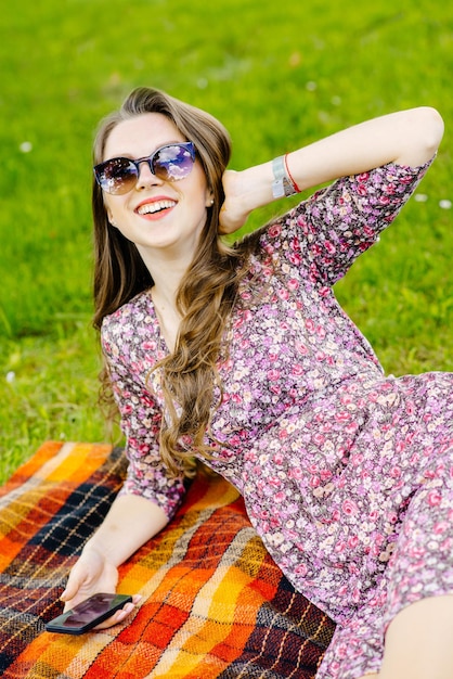 Hermosa chica con gafas de sol con teléfono relajándose en el césped del parque