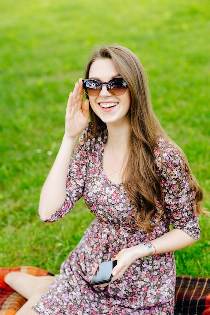 Hermosa chica con gafas de sol con teléfono relajándose en el césped del parque