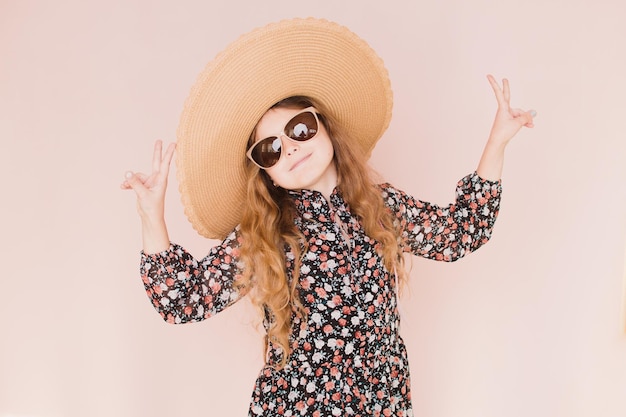 Hermosa chica con gafas y un sombrero sobre un fondo rosa