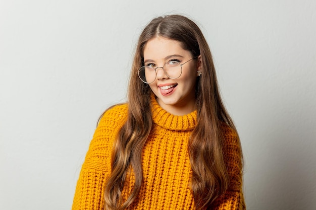 Hermosa chica con gafas y suéter amarillo sobre fondo blanco.