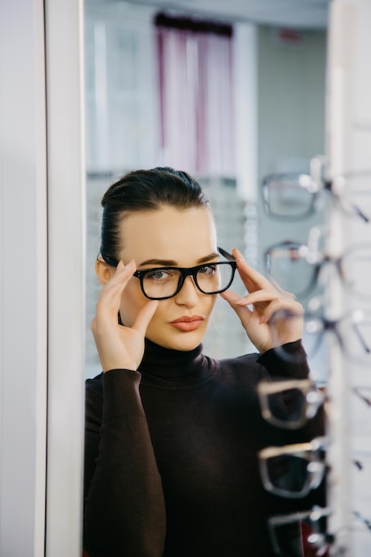 Hermosa chica con gafas en la tienda de óptica Corrección de la vista Óptica Emociones Oftalmología