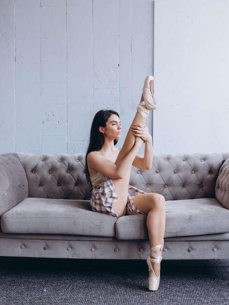 Hermosa chica gimnasta en casa realiza ejercicios en el sofá