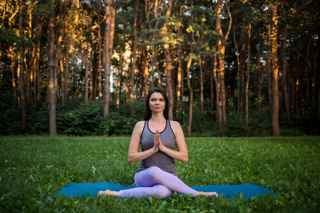 Hermosa chica haciendo yoga en el parque al atardecer