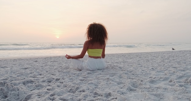 Hermosa chica haciendo yoga en la playa.