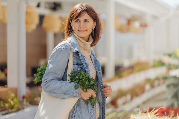 Hermosa chica con hierbas y verduras en una bolsa ecológica de algodón cerca de un pajar en una feria. Cosecha de otoño.