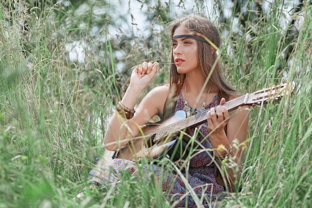 Hermosa chica hippie con guitarra sentada en el claro del bosque