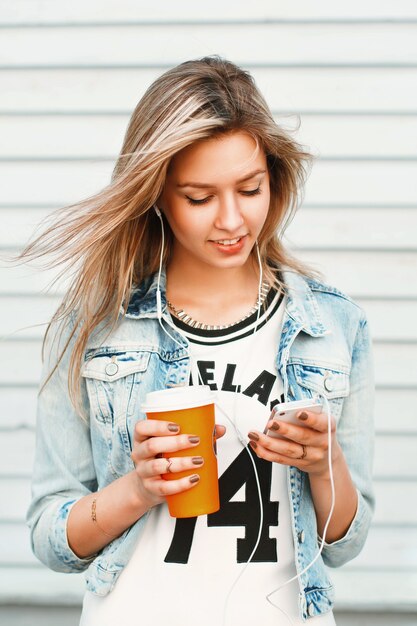 Hermosa chica hipster feliz escucha música en el teléfono y tomando café