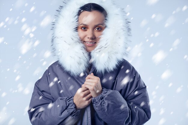 Hermosa chica hispana encantadora en abrigo azul con nieve que cae