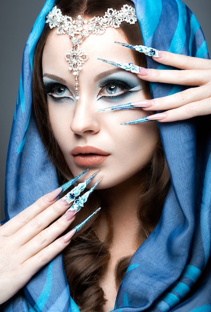 Hermosa chica en imagen árabe oriental con uñas largas y maquillaje azul brillante. Fotografía tomada en el estudio sobre un fondo gris