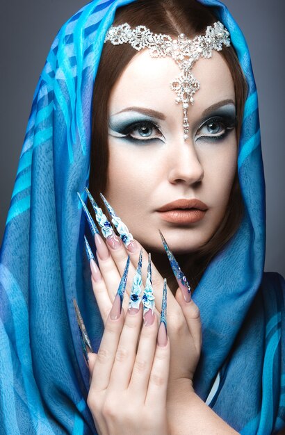 Hermosa chica en imagen árabe oriental con uñas largas y maquillaje azul brillante. Fotografía tomada en el estudio sobre un fondo gris