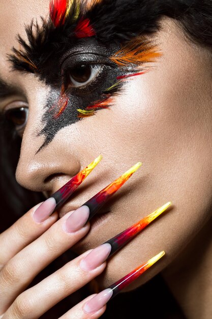 Hermosa chica en imagen de ave fénix con maquillaje creativo y uñas largas Diseño de manicura cara de belleza