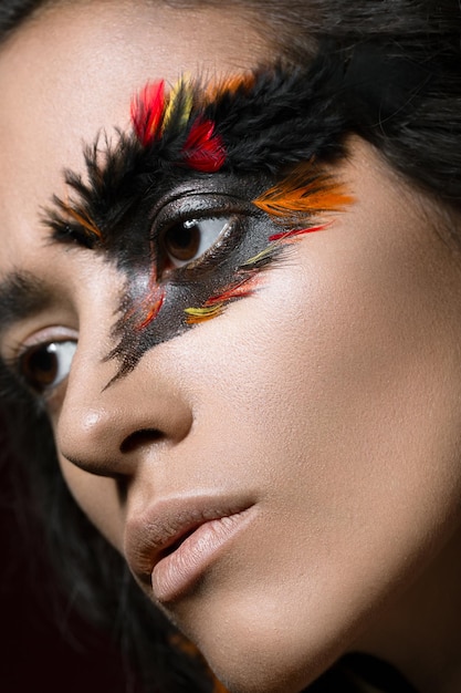 Hermosa chica en la imagen del pájaro Fénix con cara de belleza de maquillaje creativo