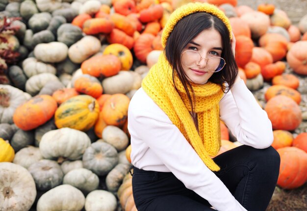 Hermosa chica en el jardín de otoño con calabazas amarillas